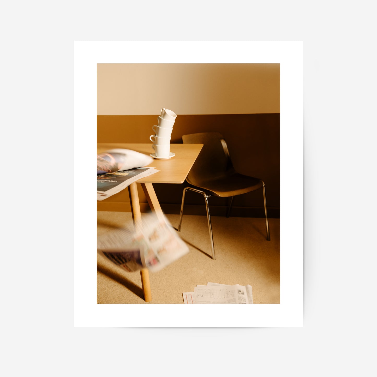 A serene minimalistic setting featuring a wooden desk with stacked cups, a chair, and scattered papers, evoking simplicity and calmness.